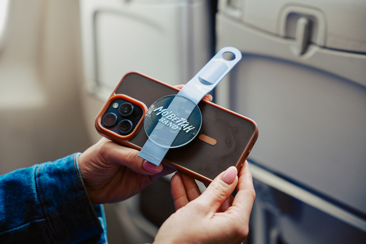 Person holding a phone with Mo'Bettah band on it inside a plane