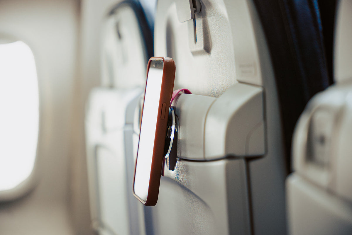 Pink Mo'Bettah Airplane Phone Holder holding an iPhone on an airplane seat pocket during a flight
