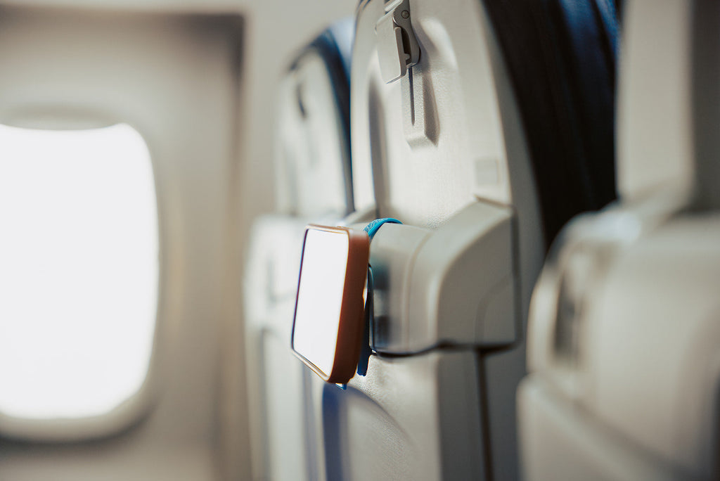 Blue Mo'Bettah Airplane Phone Holder holding an iPhone on an airplane seat pocket during a flight