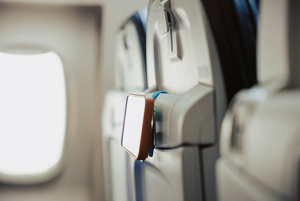 Blue Mo'Bettah Airplane Phone Holder holding an iPhone on an airplane seat pocket during a flight