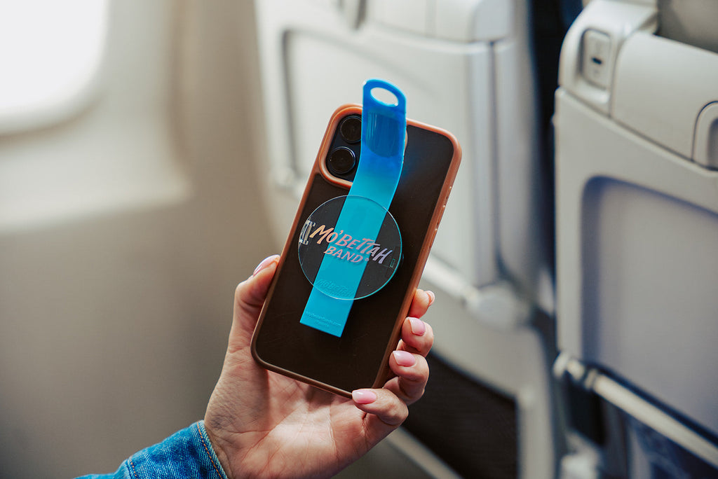 Traveler holding a Blue Mo'Bettah Airplane Phone Holder next to a MagSafe-compatible iPhone