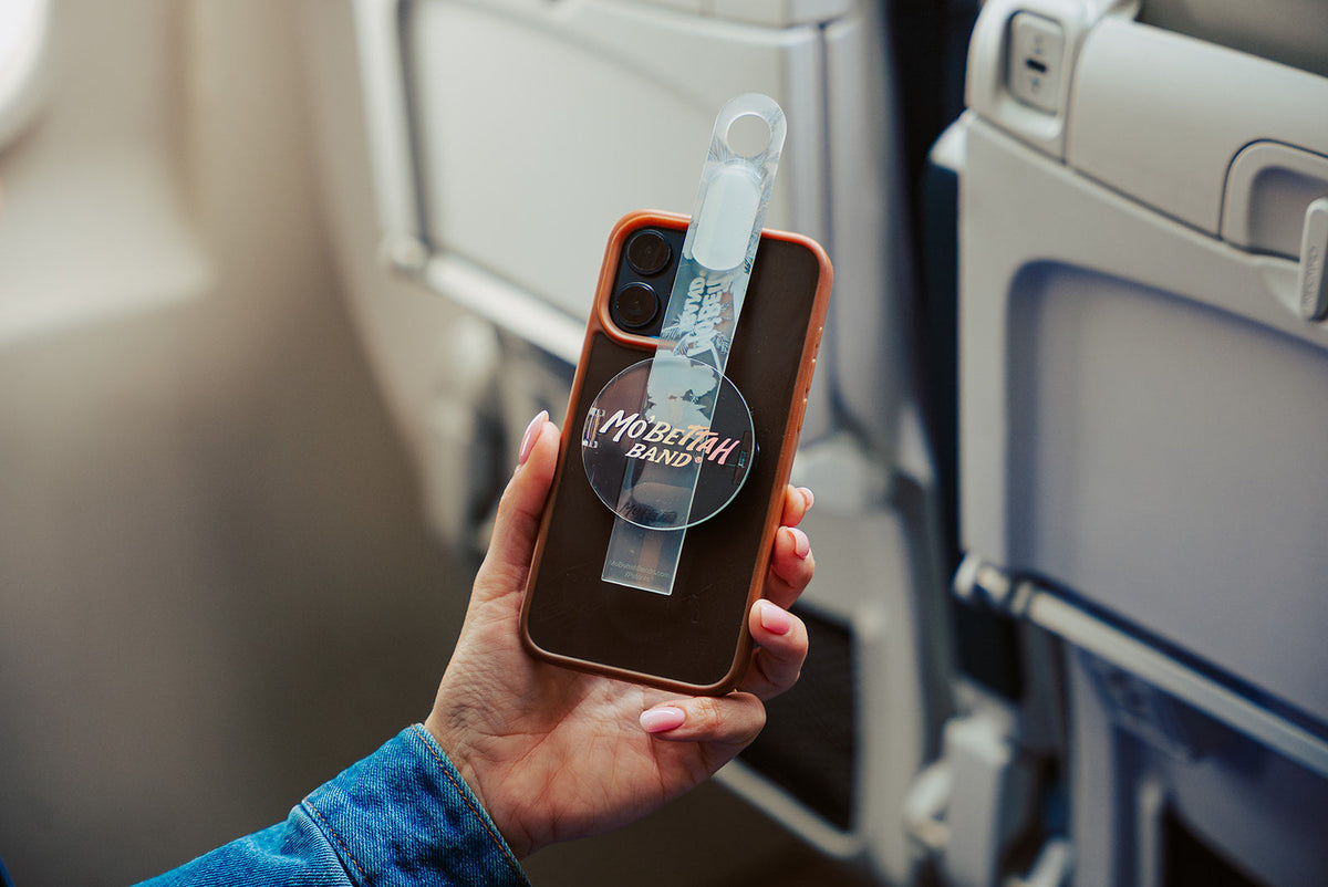 Traveler holding a Clear Mo'Bettah Airplane Phone Holder next to a MagSafe-compatible iPhone