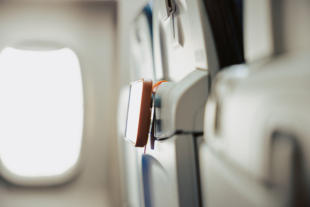 Orange Mo'Bettah Airplane Phone Holder holding an iPhone on an airplane seat pocket during a flight