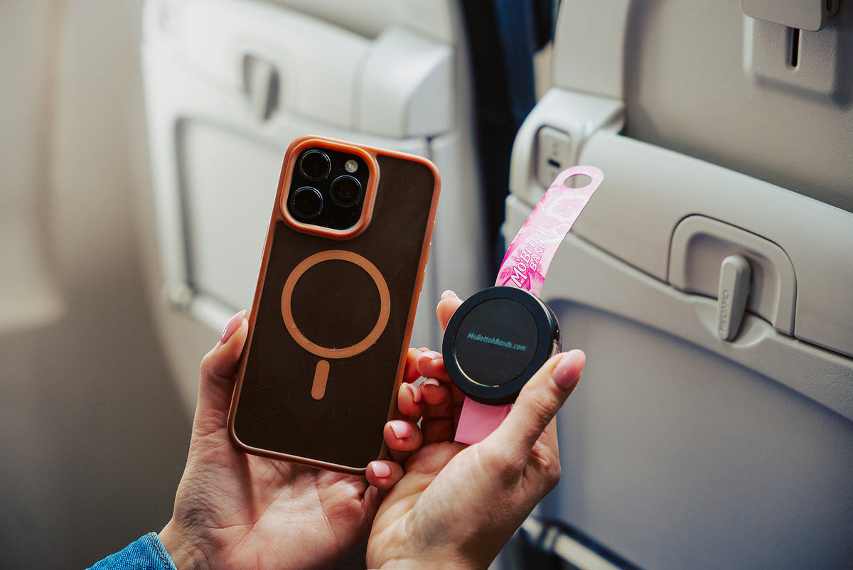 Traveler holding a Pink Mo'Bettah Airplane Phone Holder next to a MagSafe-compatible iPhone