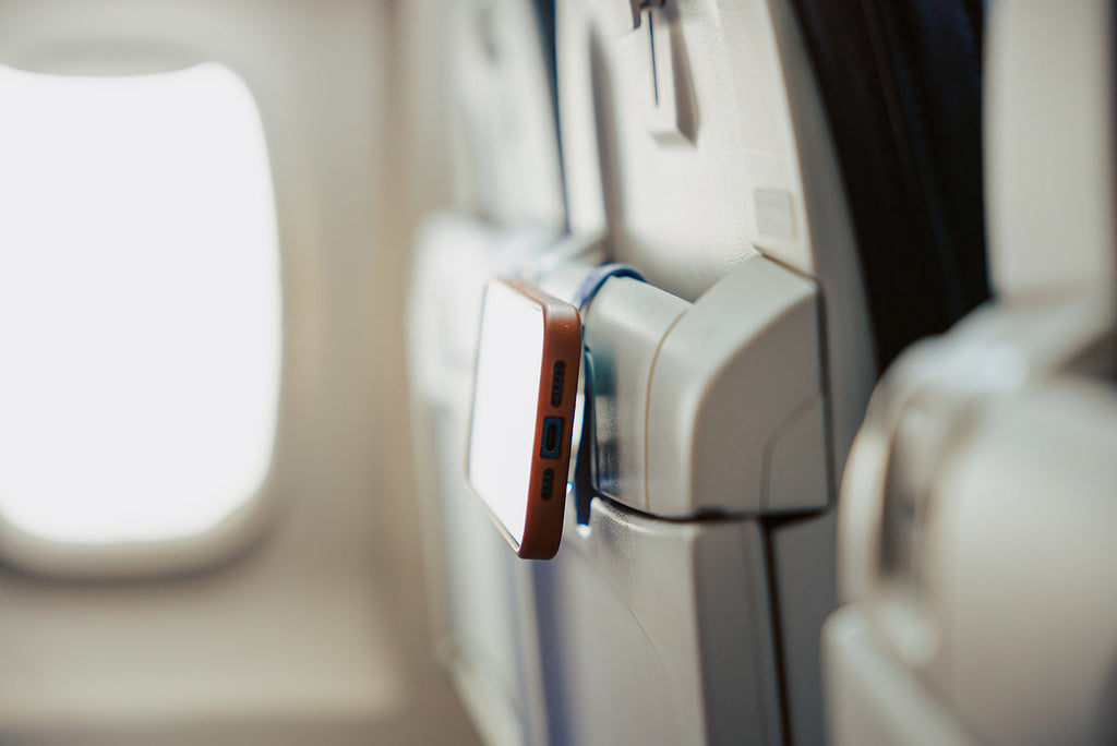Purple Mo'Bettah Airplane Phone Holder holding an iPhone on an airplane seat pocket during a flight