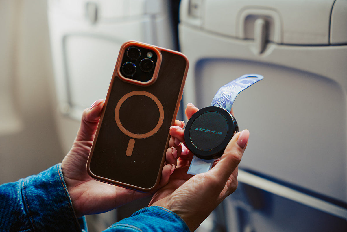 Traveler holding a Purple Mo'Bettah Airplane Phone Holder next to a MagSafe-compatible iPhone